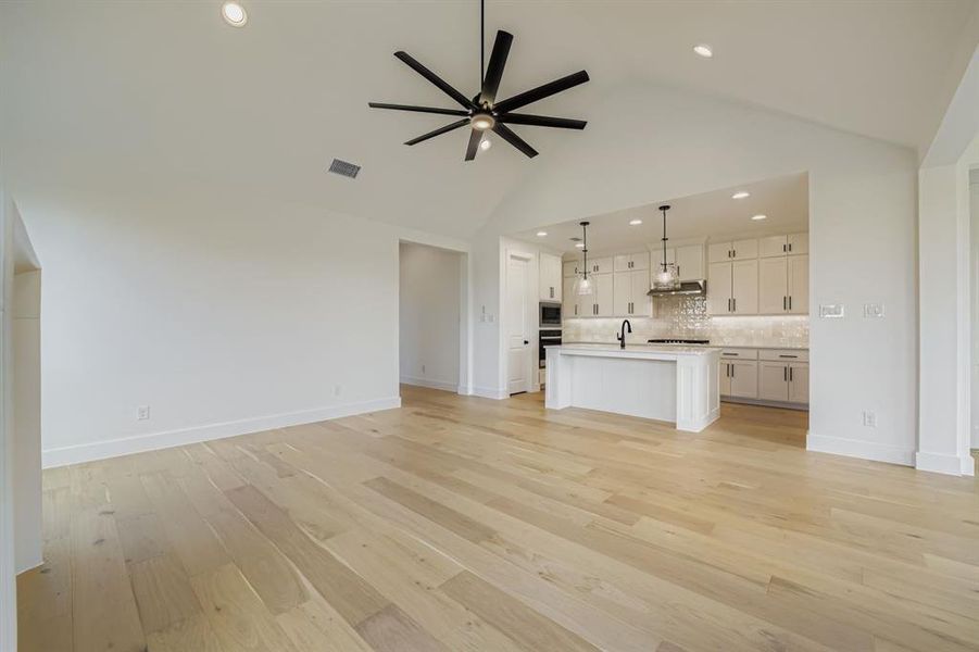 Unfurnished living room featuring light wood-style floors, a ceiling fan, recessed lighting, and high vaulted ceiling Unfurnished living room featuring light wood-style floors, a ceiling fan, recessed lighting, and high vaulted ceiling