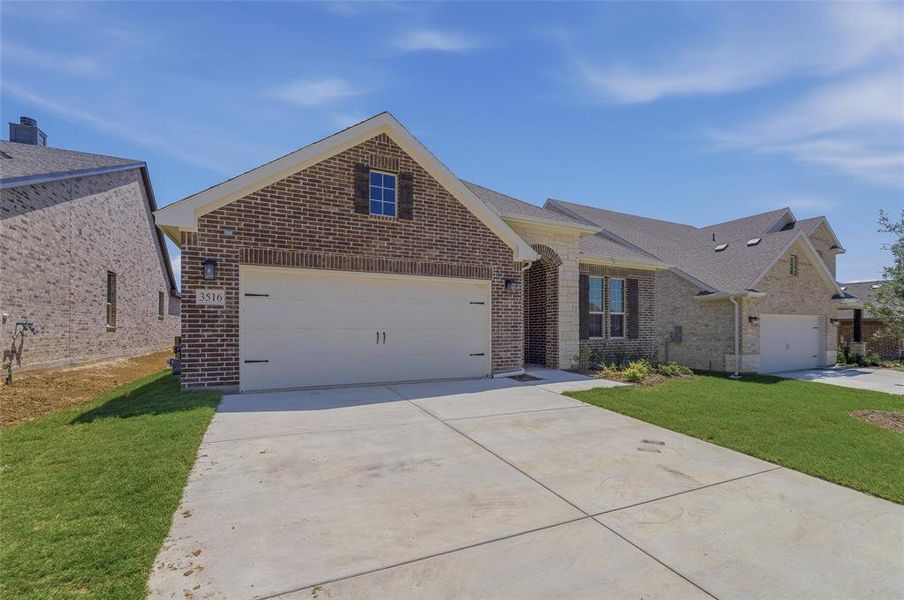 Brick and stone facade residence featuring a two-car garage, concrete driveway, and dormer window with decorative shutters Brick and stone facade residence featuring a two-car garage, concrete driveway, and dormer window with decorative shutters