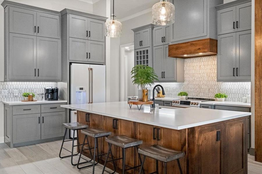 Kitchen featuring pretty tile backsplash, tall & deep cabinets, ornamental molding, an island with sink, and pendant lighting