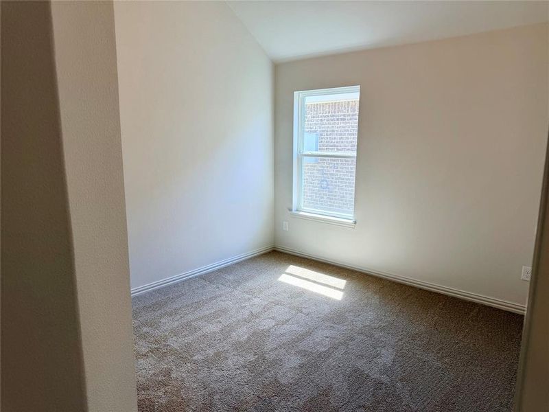 Neutral-toned room featuring a single window, vaulted ceiling, plush carpet flooring, and white baseboards