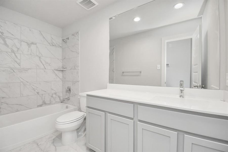 The secondary bath includes modern tile flooring, a combined bath and shower with a tile surround, light wood cabinetry, and a beautiful light-colored countertop.