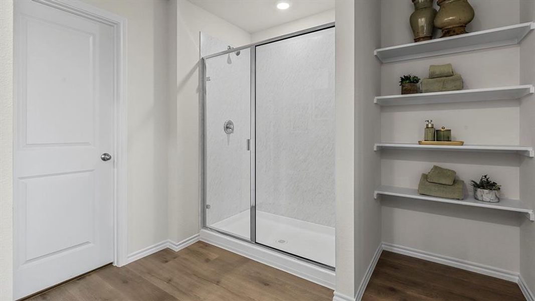 The bathroom features wood-look flooring, a glass-enclosed shower, and built-in shelving