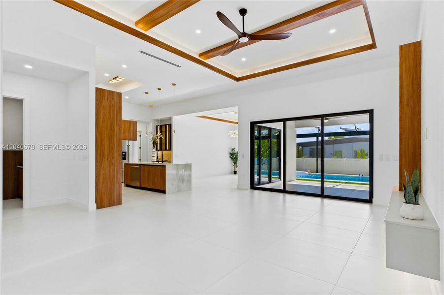 Spacious great room features soaring tray ceilings, designer wood accents, and oversized impact sliders that seamlessly connect indoor and outdoor living