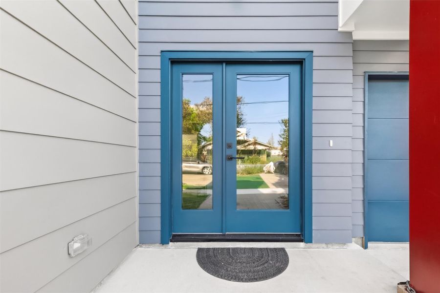 A bold set of glass-panel French doors in a standout color sets the tone for this contemporary home. The covered entry provides a welcoming transition into the open foyer, a small detail that speaks to the care taken throughout this new construction.