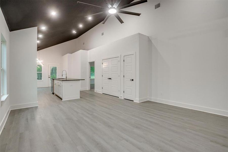 Unfurnished living room featuring ceiling fan, light wood-type flooring, and high vaulted ceiling