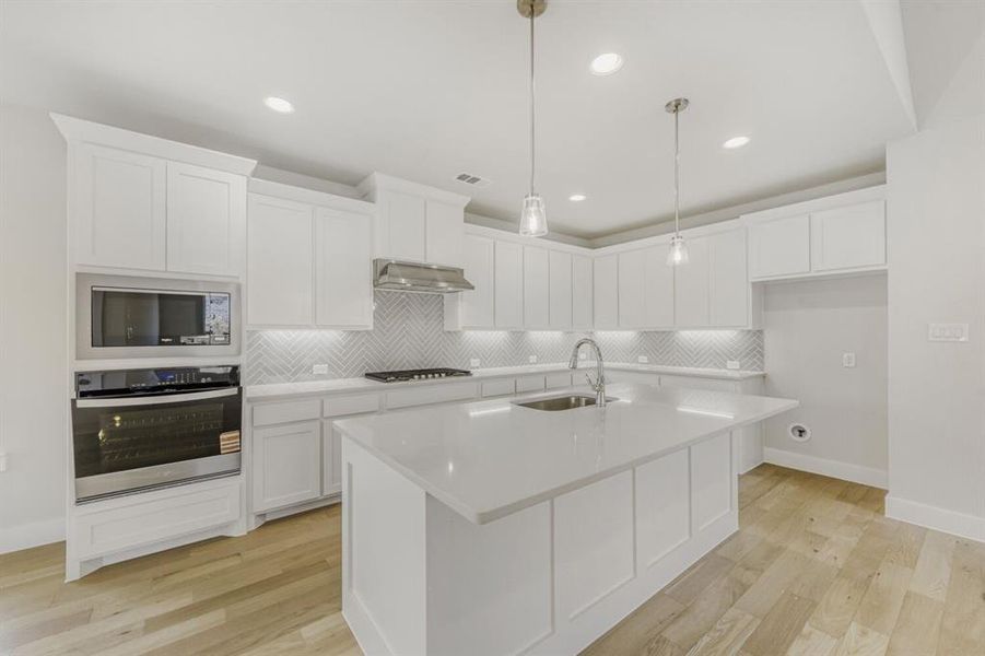 Kitchen with stainless steel appliances, light wood-style floors, white cabinets, a kitchen island with sink, and pendant lighting
