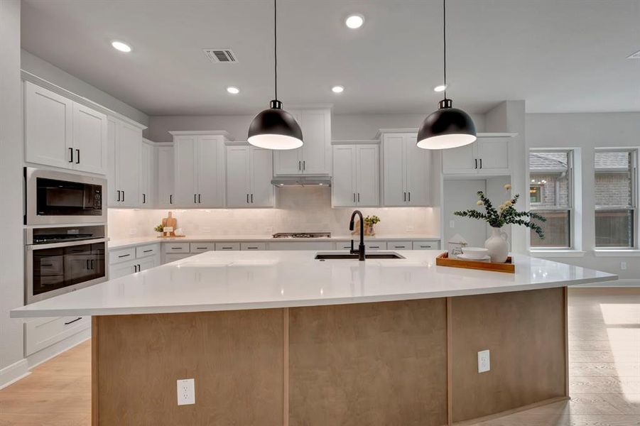 Kitchen with light wood finished floors, stainless steel appliances, a spacious island, hanging light fixtures, and two tone cabinets