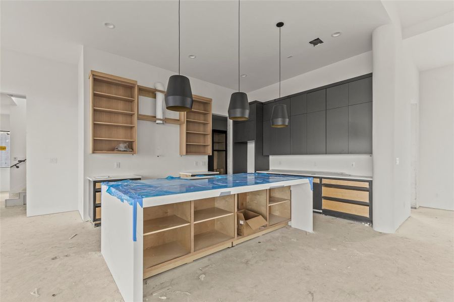 Spacious kitchen featuring an expansive center island, modern pendant lighting, matte black upper cabinetry, and natural wood-tone lower cabinetry