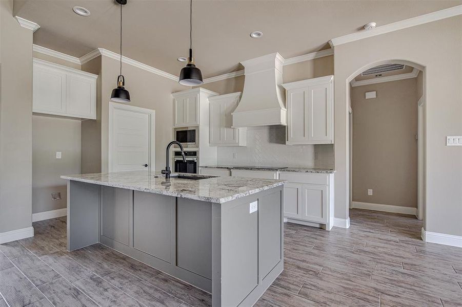 Kitchen featuring appliances with stainless steel finishes, white cabinets, a center island with sink, and custom range hood