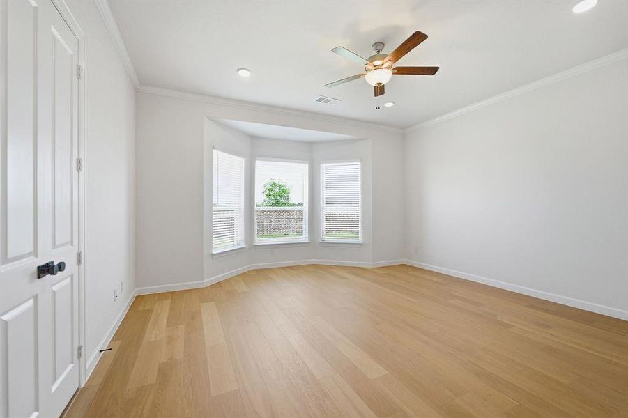 Spacious room featuring light wood-finish flooring, a bay window with blinds, recessed lighting, a ceiling fan with integrated light, and crown molding