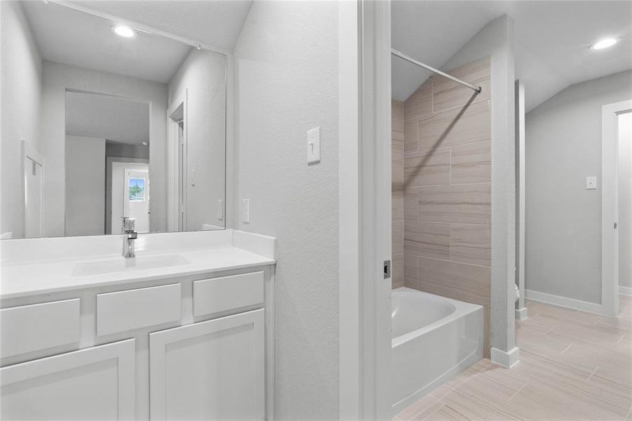 Secondary bath is a jack and jill bathroom featuring tile flooring, bath/shower combo with tile surround, white stained wood cabinets, beautiful light countertops, mirror, sleek fixtures and modern finishes.