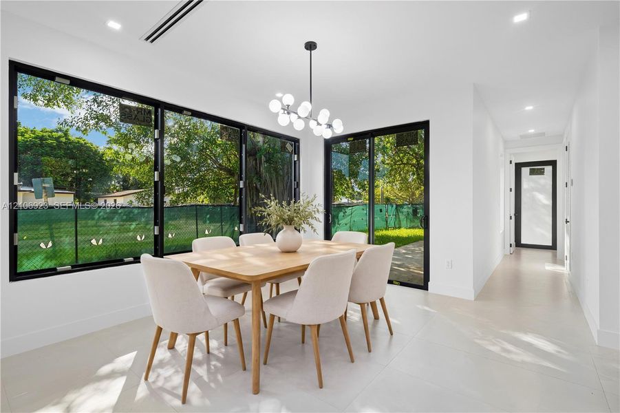 Dining area featuring expansive floor-to-ceiling black-framed windows, integrated recessed lighting, a modern multi-globe chandelier, and porcelain tile flooring Dining area featuring expansive floor-to-ceiling black-framed windows, integrated recessed lighting, a modern multi-globe chandelier, and porcelain tile flooring