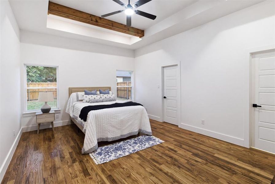 Spacious room featuring wood-finish flooring, a tray ceiling with exposed beam accent, and a ceiling fan