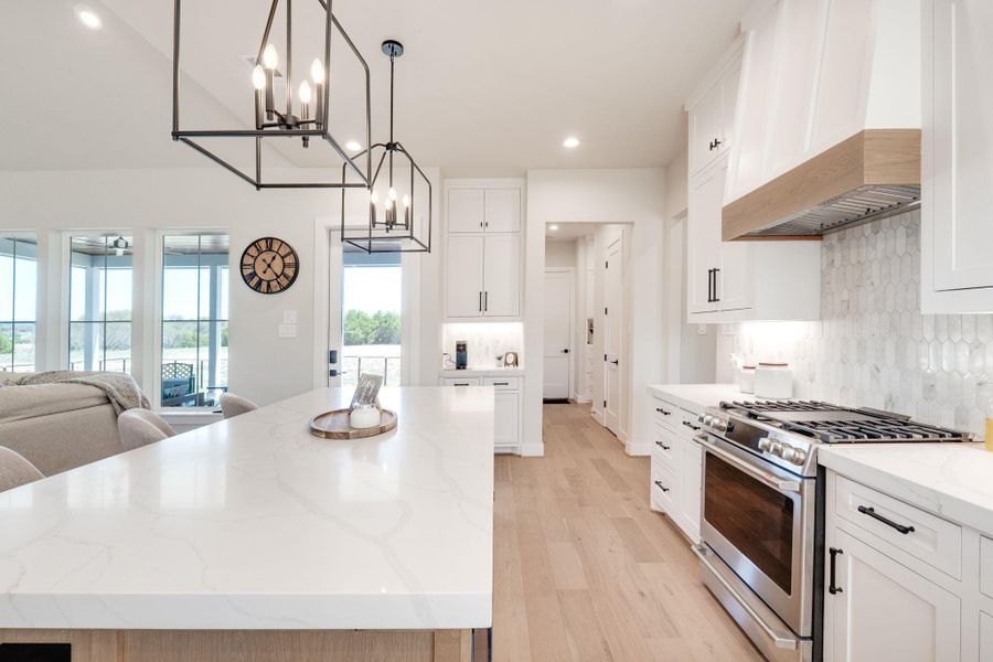 Kitchen with gas stove, hanging lights, tasteful backsplash, and white cabinets