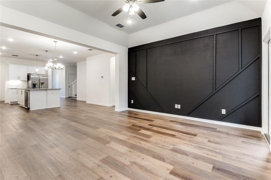 Unfurnished living room featuring ceiling fan with notable chandelier and light hardwood / wood-style floors