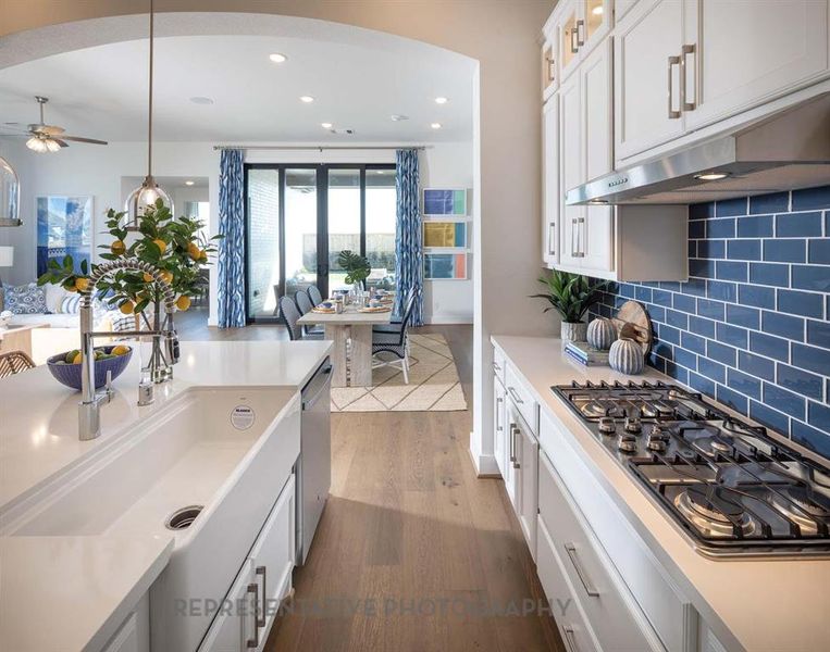 Kitchen with white cabinetry, appliances with stainless steel finishes, hanging light fixtures, glass insert cabinets, and dark wood-style floors Kitchen with white cabinetry, appliances with stainless steel finishes, hanging light fixtures, glass insert cabinets, and dark wood-style floors