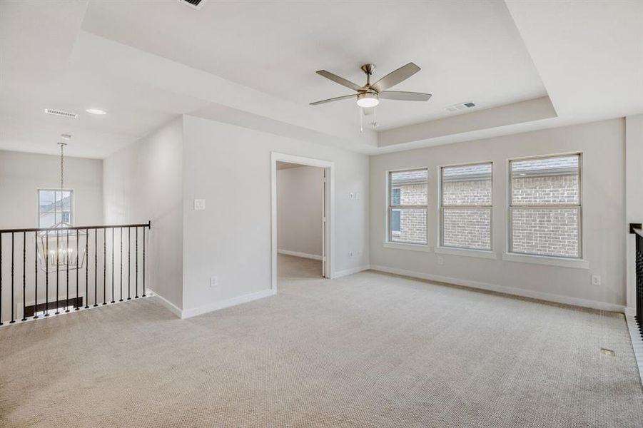 Unfurnished room featuring a raised ceiling, ceiling fan, light carpet, and hanging lights
