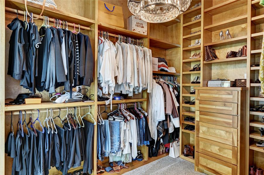 This spacious walk-in closet features custom wood shelving, ample hanging space, and a built-in drawer unit. The elegant chandelier adds a touch of luxury, making it both functional and stylish.