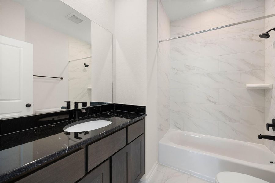 Beautifully finished full ensuite bathroom attached directly to the third secondary bedroom. This modern space features a deep bathtub and shower combination accented by bright, floor-to-ceiling white marble-patterned tile. The rich, dark vanity provides generous storage, topped with premium high-contrast black granite, an undermount sink, and contemporary matte black plumbing fixtures that perfectly complement the home's cohesive design. Beautifully finished full ensuite bathroom attached directly to the third secondary bedroom. This modern space features a deep bathtub and shower combination accented by bright, floor-to-ceiling white marble-patterned tile. The rich, dark vanity provides generous storage, topped with premium high-contrast black granite, an undermount sink, and contemporary matte black plumbing fixtures that perfectly complement the home's cohesive design.