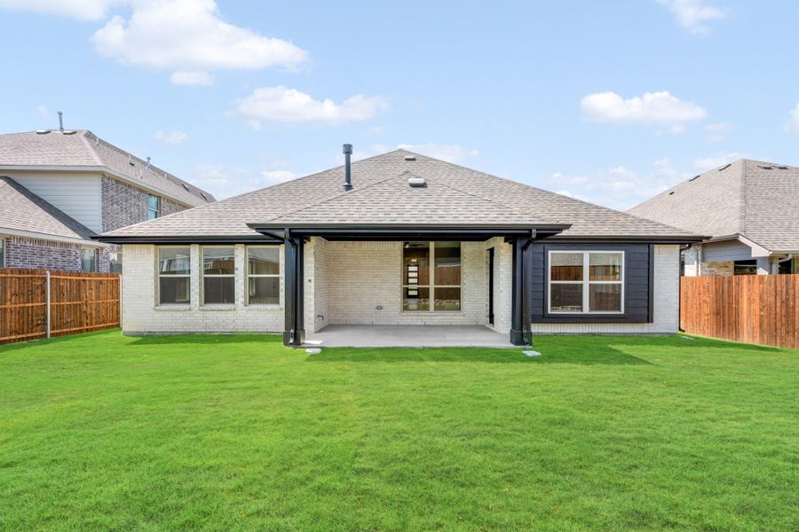 Back of single-story brick home with covered patio, dark trim accents, and fenced green backyard