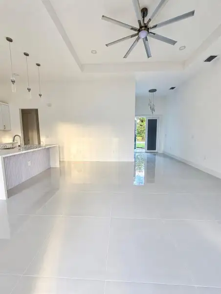 Open-concept interior featuring large-format tile flooring, tray ceilings, recessed lighting, multi-blade ceiling fan, and kitchen peninsula with vertical slat detailing