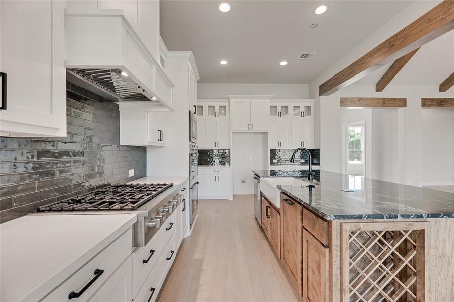 Kitchen featuring a center island with sink, beam ceiling, dark stone counters, appliances with stainless steel finishes, and backsplash