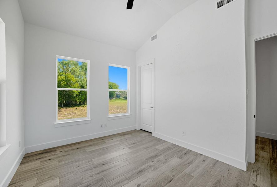 Empty room with vaulted ceiling, light wood-style flooring, and a ceiling fan Empty room with vaulted ceiling, light wood-style flooring, and a ceiling fan