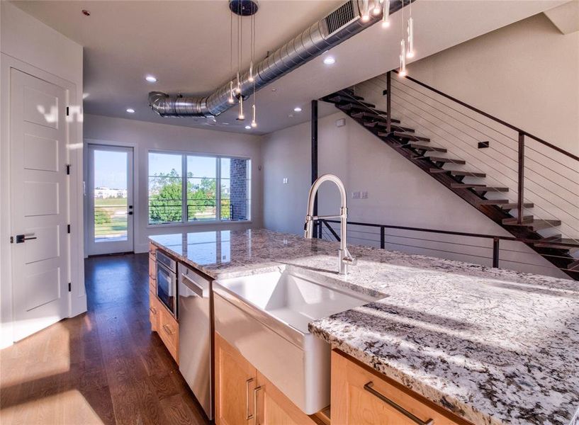 Kitchen featuring light brown cabinetry, light stone countertops, decorative light fixtures, and dark hardwood / wood-style flooring