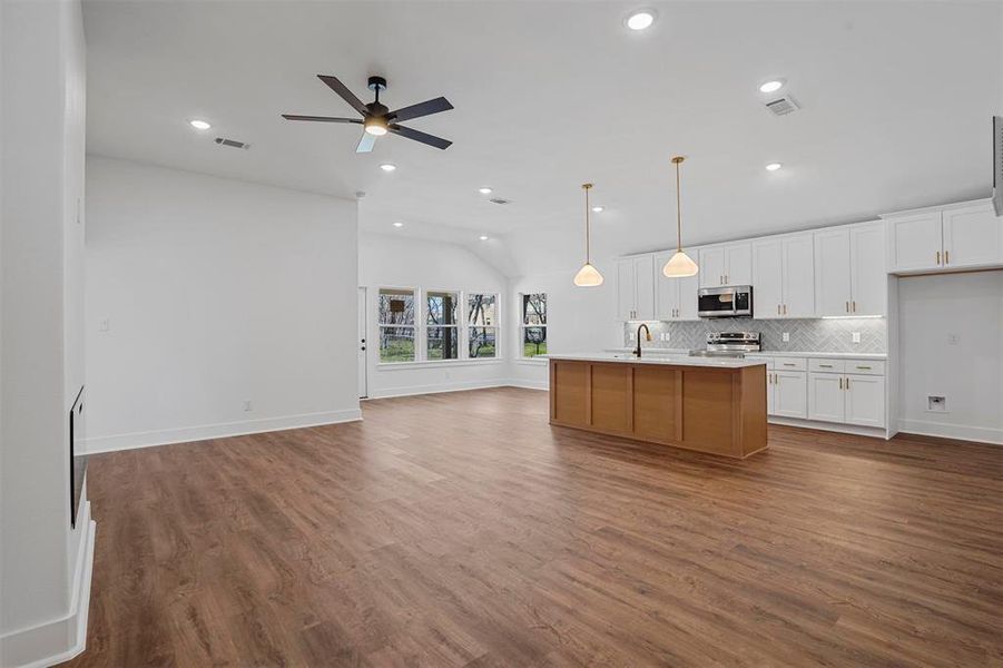 Kitchen with open floor plan, decorative backsplash, wood finished floors, stainless steel appliances, and a sink