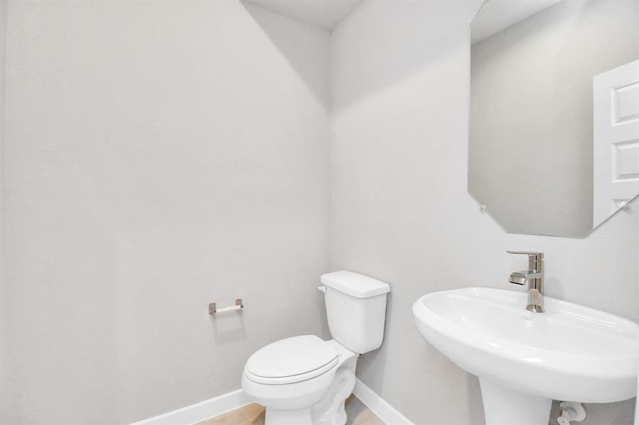 This half bathroom features a stylish pedestal sink, modern hardware, and bright recessed lighting, creating a sleek and inviting space. Sample photo of completed home with similar floor plan. Actual colors and selections may vary.