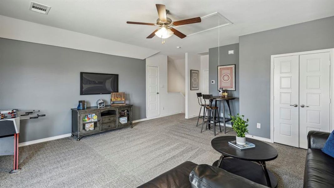 Spacious room with gray walls and patterned carpet, featuring a ceiling fan, white paneled doors, and an entertainment console