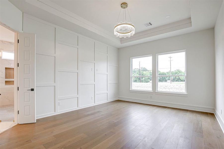 Spare room featuring a chandelier, light wood-type flooring, and a tray ceiling