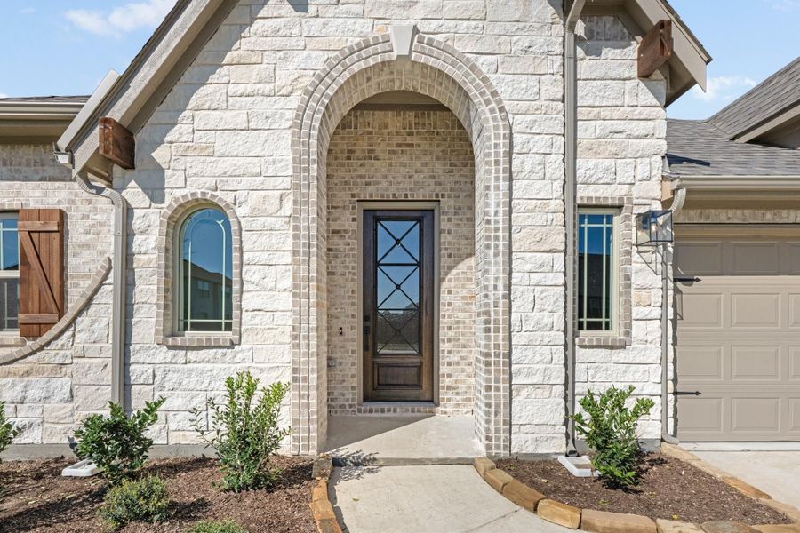 Home entrance with arched brick surround, wood and glass front door, and light stone exterior facade.