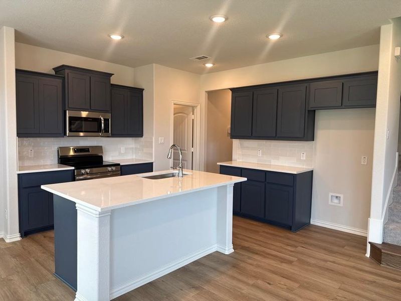 Modern kitchen featuring dark blue cabinetry, light-toned countertops, and a subway tile backsplash Modern kitchen featuring dark blue cabinetry, light-toned countertops, and a subway tile backsplash