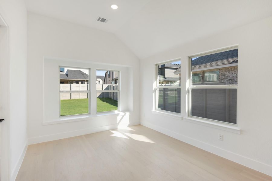 Empty room with vaulted ceiling, light wood floors, and large windows overlooking backyard