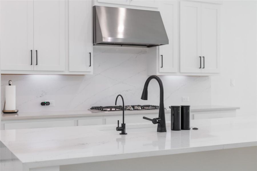 Kitchen with backsplash, white cabinets, light stone counters, and exhaust hood