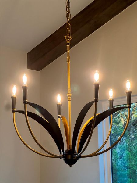 A classic brass chandelier hangs elegantly below a rich exposed wooden ceiling beam. A classic brass chandelier hangs elegantly below a rich exposed wooden ceiling beam.