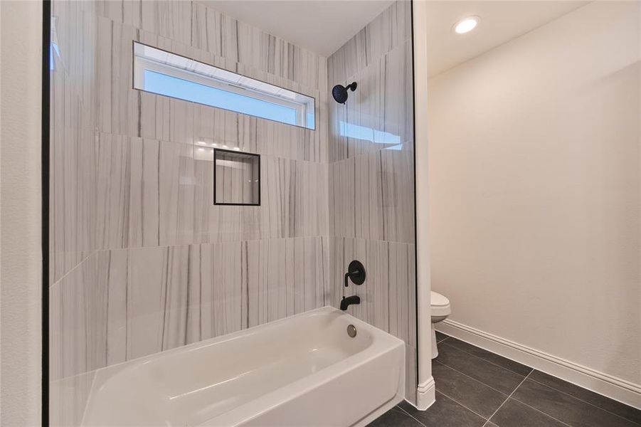 Bathroom featuring tiled shower / bath combo, toilet, and tile patterned floors