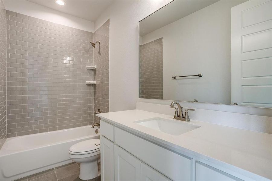 Full bathroom with tiled shower / bath combo, toilet, tile patterned floors, and vanity