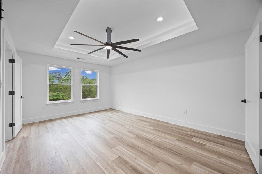 Spacious room featuring wood-finish flooring, a tiered tray ceiling with recessed lighting, and a modern ceiling fan Spacious room featuring wood-finish flooring, a tiered tray ceiling with recessed lighting, and a modern ceiling fan