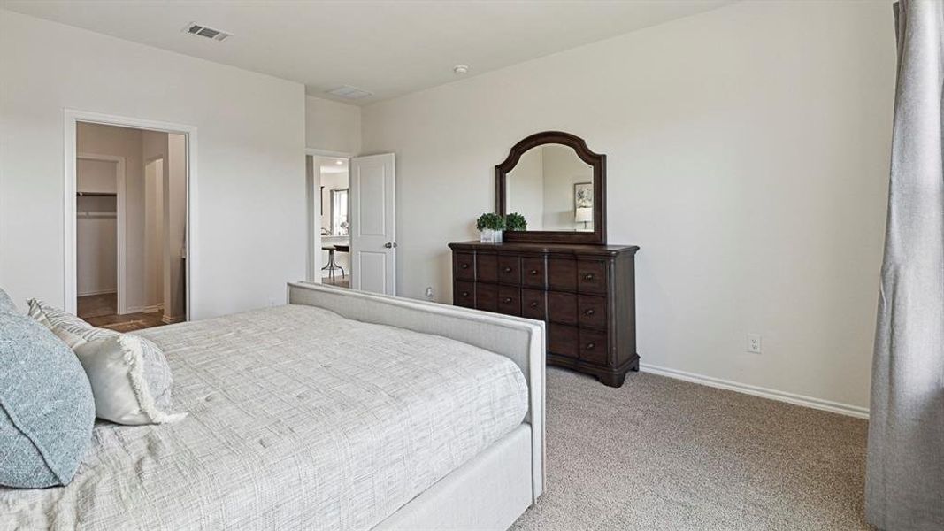 Bedroom featuring light-colored walls, carpeted floors, and a dresser with an arched mirror