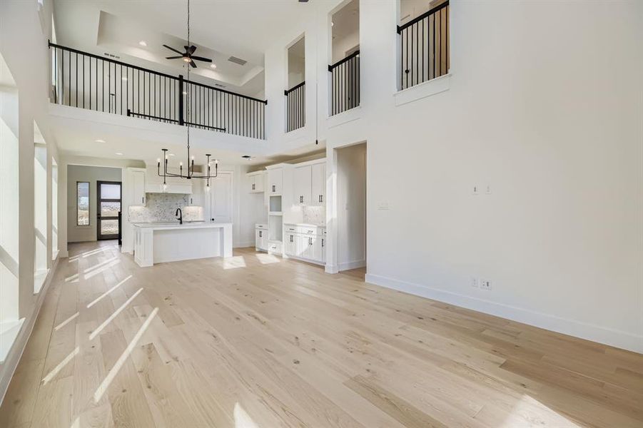 Unfurnished living room featuring light wood-type flooring, a ceiling fan, and a high ceiling Unfurnished living room featuring light wood-type flooring, a ceiling fan, and a high ceiling