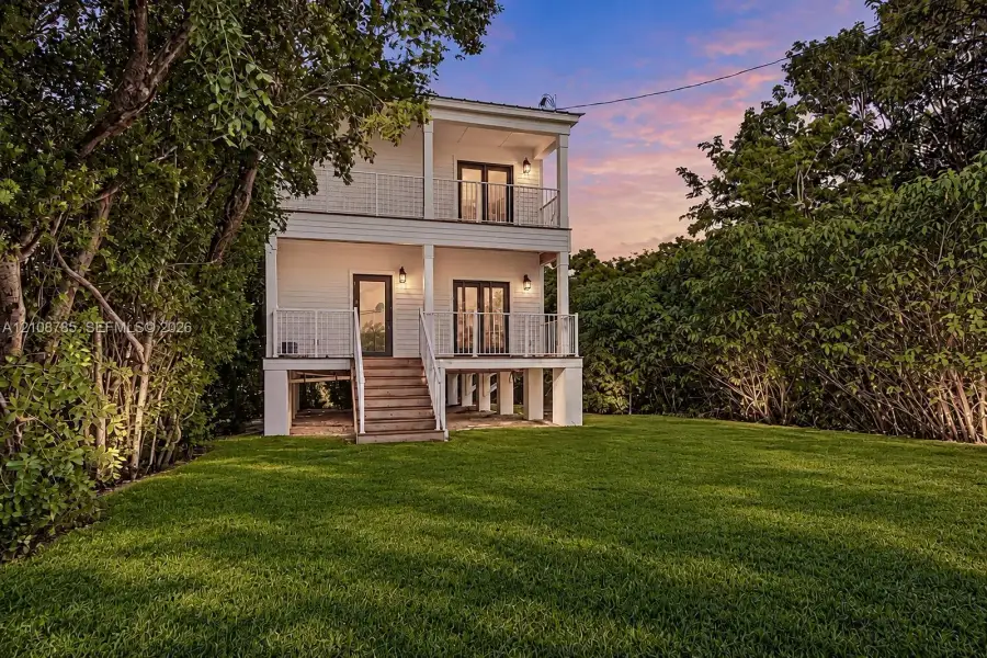 Two-story exterior featuring white horizontal siding, double-level covered porches with metal railings, a raised pier foundation, and glass-paneled exterior doors Two-story exterior featuring white horizontal siding, double-level covered porches with metal railings, a raised pier foundation, and glass-paneled exterior doors