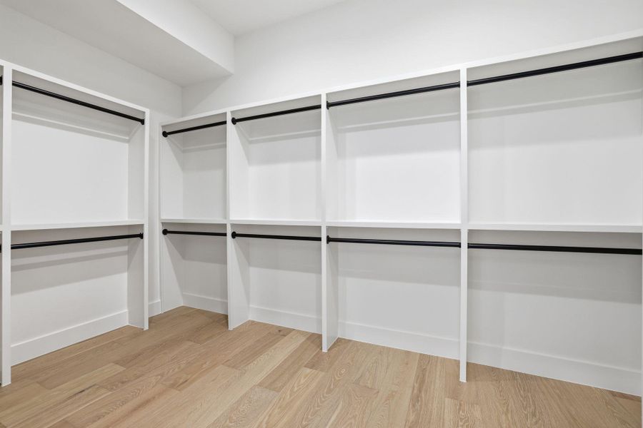 Custom closet system featuring white shelving units, black metal hanging rods, and wood-finish flooring