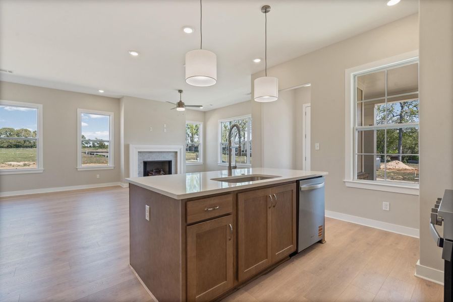 Kitchen featuring a center island with sink, pendant lighting, a fireplace, open floor plan, and light wood finished floors