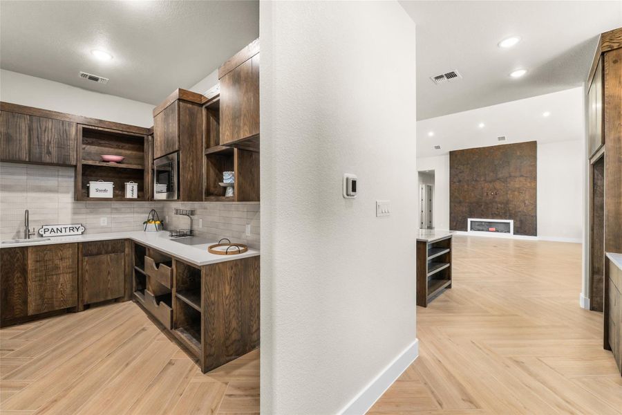 Kitchen featuring backsplash, open shelves, light stone countertops, dark brown cabinets, and recessed lighting