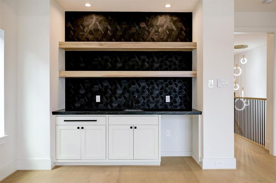 Chic wet bar in the entertainment space, featuring sleek cabinetry and designer tile backsplash. Sample image from our model home with identical layout and finishes.