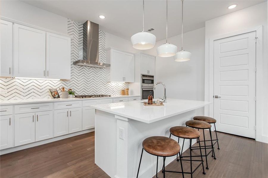 Kitchen featuring tasteful backsplash, wall chimney range hood, a kitchen island with sink, white cabinetry, and wood-type flooring