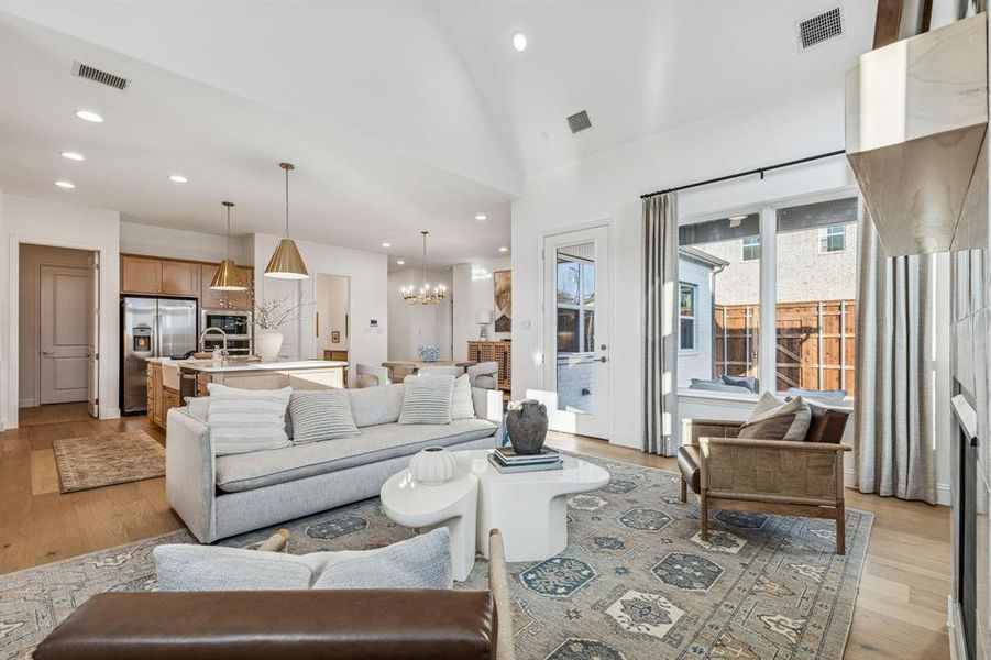 Living room with light wood-type flooring, suspended lighting, and vaulted ceiling