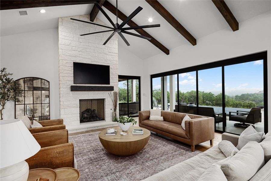 Living room with a stone fireplace, high vaulted ceiling, and beamed ceiling